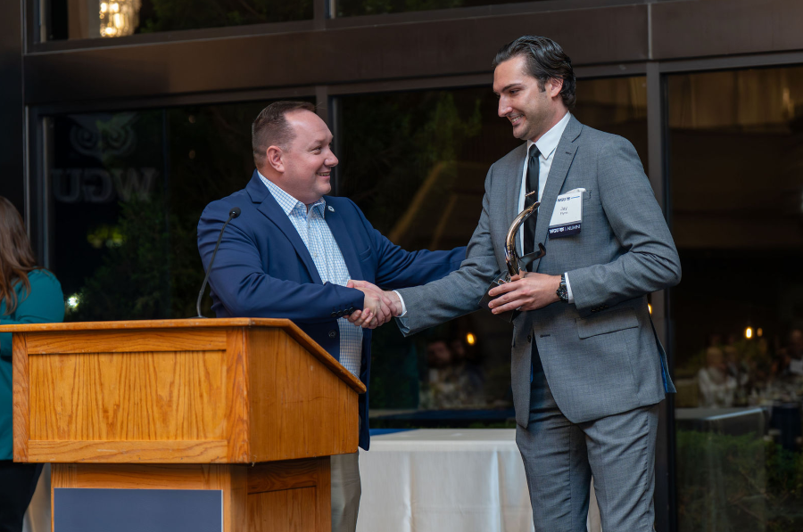 Two men shaking hands on stage, one receiving an award while standing at a podium.